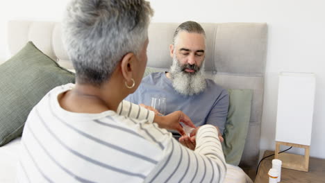 handing medication, woman caring for senior man in bed with glass of water