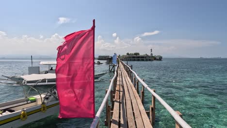 Wooden-Boardwalk-with-Colorful-Flags-Blowing-in-the-Wind-and-Boats-Docked-on-the-Side-Leading-up-to-Nalusuan-Island,-Mactan,-Cebu,-Philippines