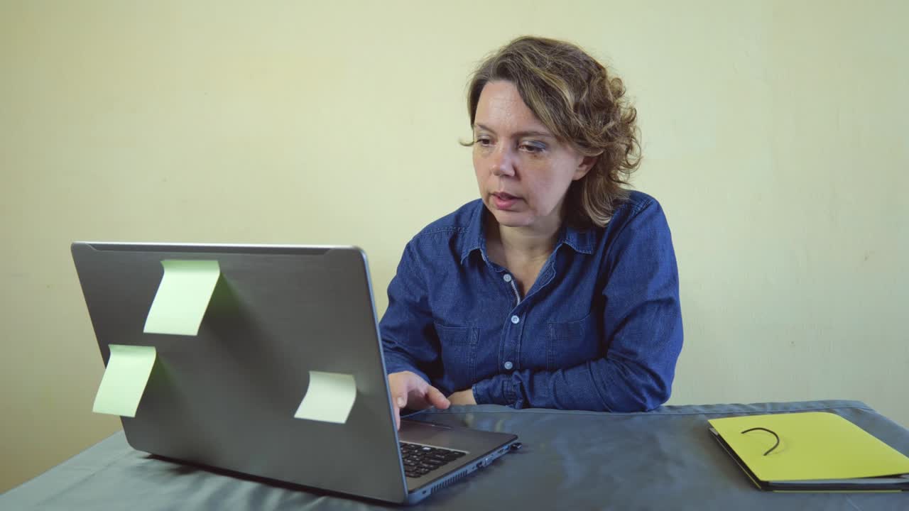 A forty-year-old woman in a denim shirt works at a laptop. Woman adult freelancer