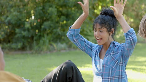 Happy-diverse-group-of-teenage-friends-sitting-on-grass-and-talking-in-sunny-park,-slow-motion