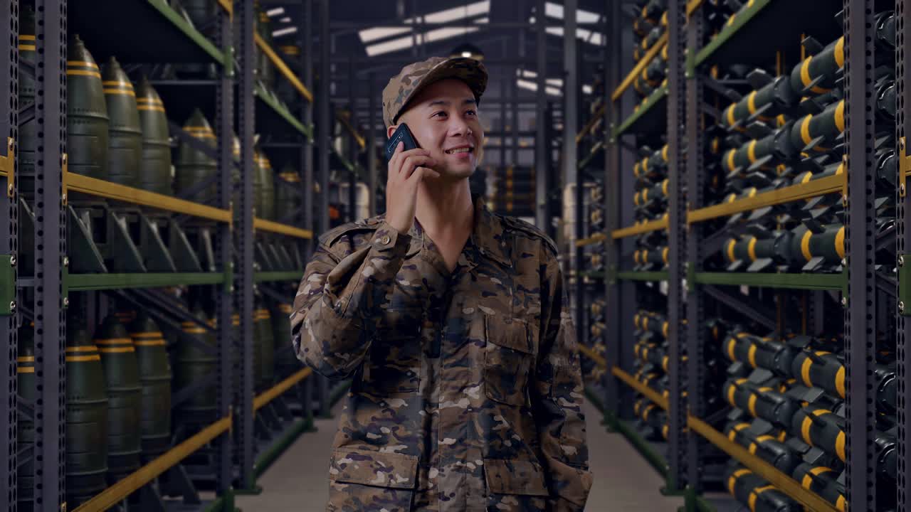 Soldato asiatico che parla al telefono e si guarda intorno mentre si trova in un magazzino di munizioni militari