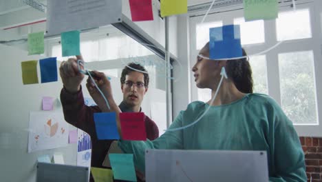 man and woman discussing over memo notes on glass board at office