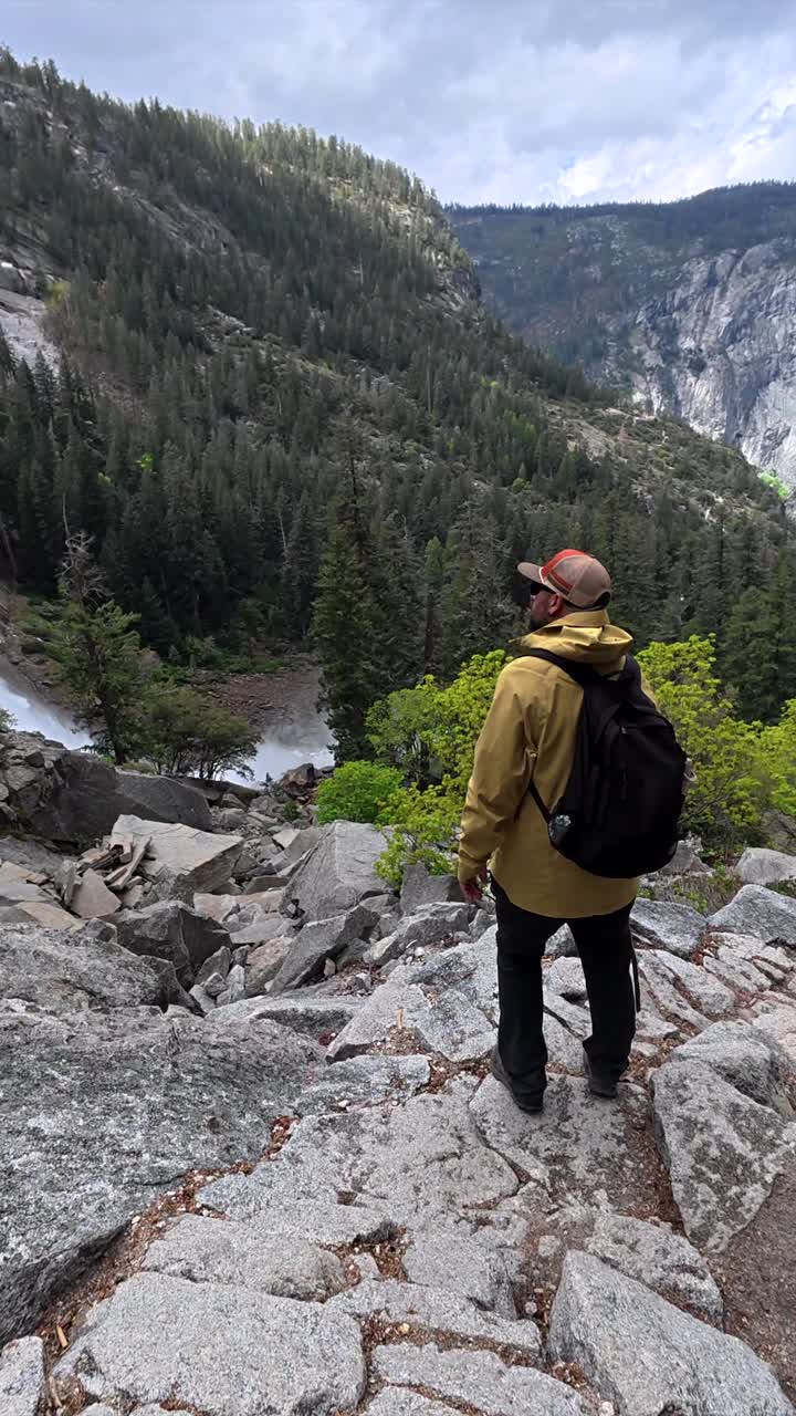 Uomo che scende un sentiero di montagna roccioso verso una cascata