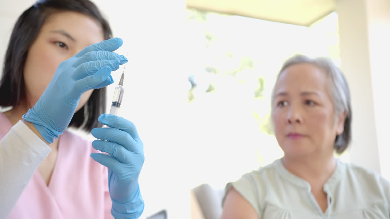 Nurse preparing syringe while senior asian woman watching attentively at home