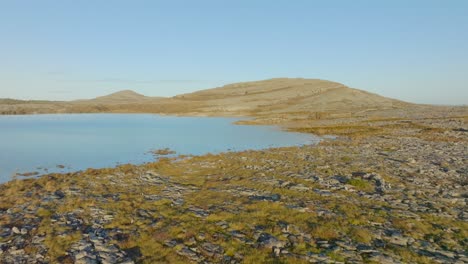 low aerial dolly above grassy meadows and limestone rocks to flooded lake water edge, burren ireland