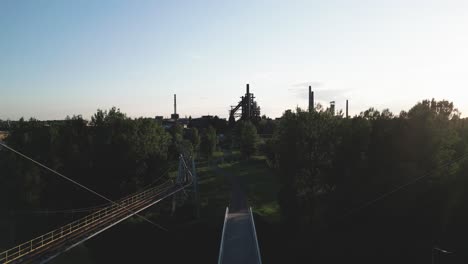 A-camera-flying-backwards-reveals-a-panorama-of-an-old-industrial-blast-furnace-on-the-horizon-and-a-modern-cable-stayed-pedestrian-bridge