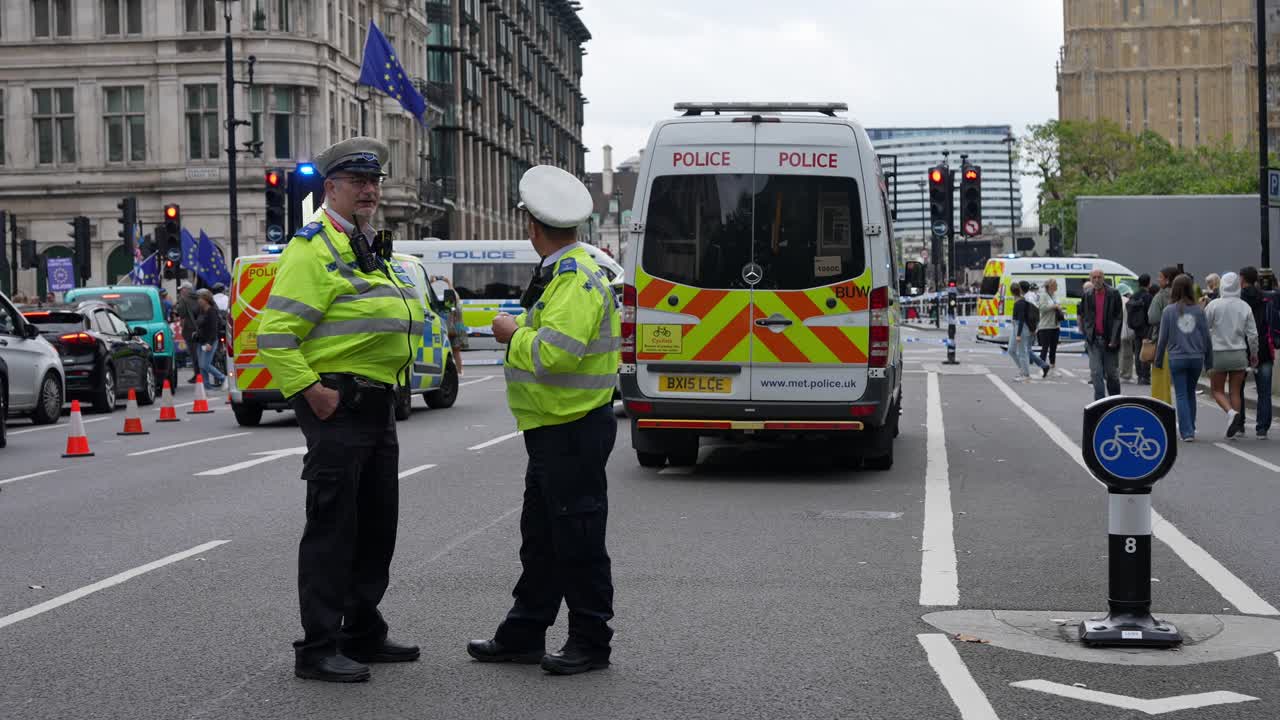 Two police officers stand in front of a van and red and white traffic cones marking the start of a cordon at the scene of a major incident on Parliament Square.