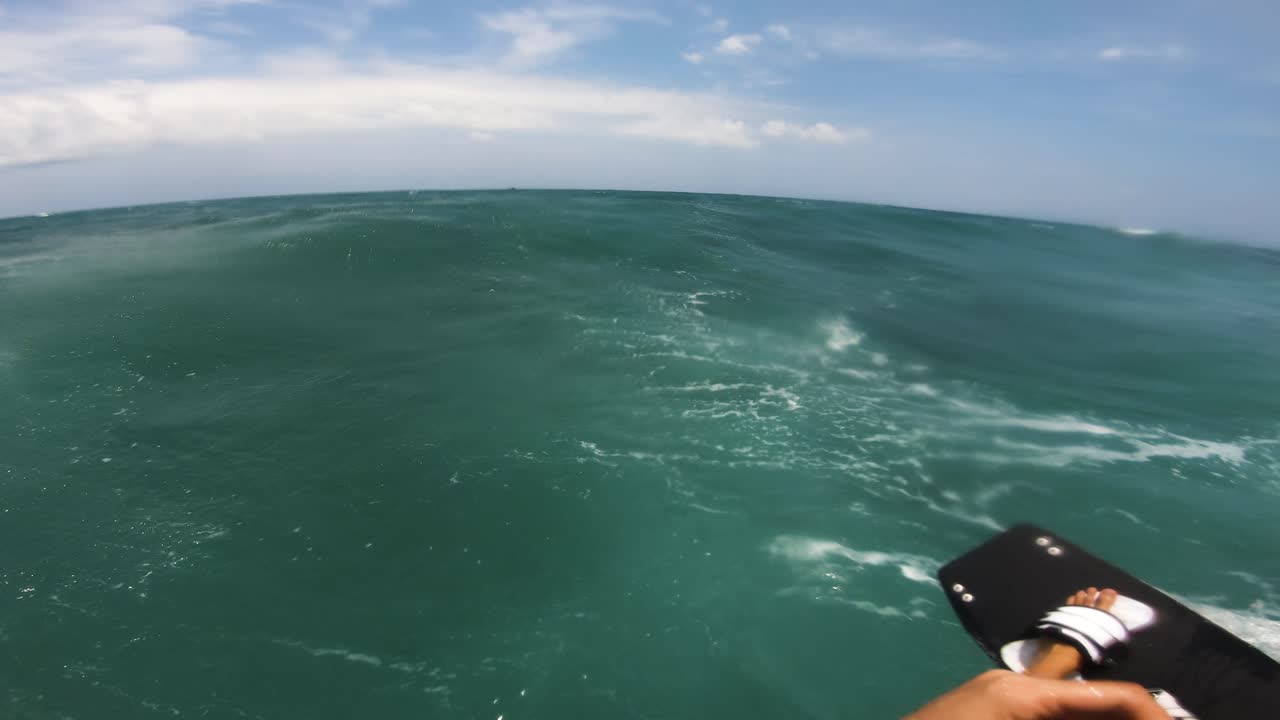 Pov shot of kite surfer jumping over high waves during dramatic cloudscape in background.