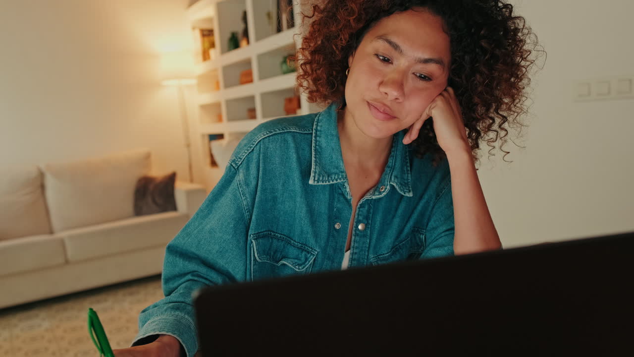 Pensive Young Woman Studying on Laptop and Taking Notes at Home