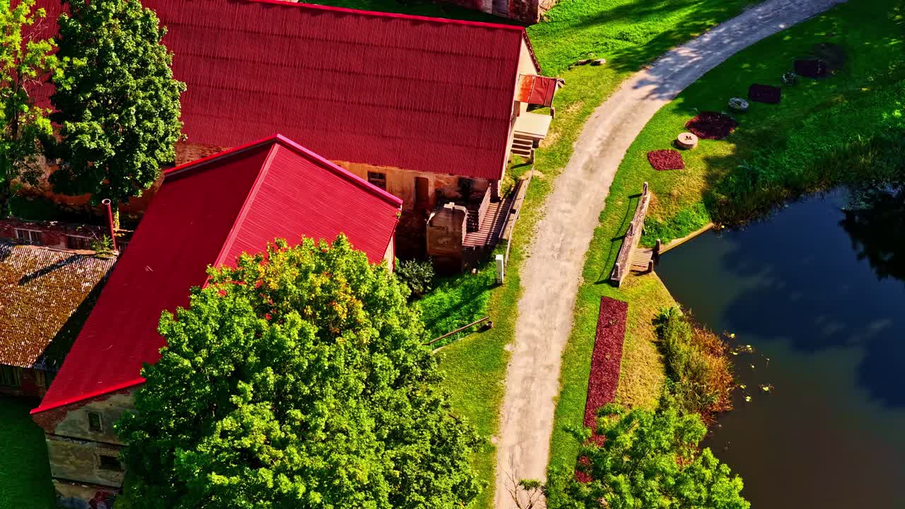 Aerial glides over Jaunpils Castle nestled in foliage with river visible in lower frame, push in tilt down