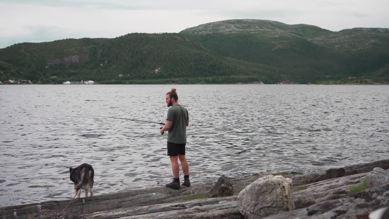 un hombre pescando en un lago con su mascota perro durante un día nublado
