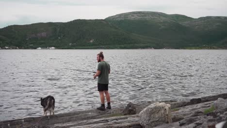 a man fishing on a lake with his dog pet during cloudy day