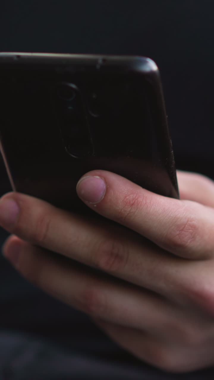 Person hand scrolls news feed on mobile phone sitting at laptop while works in semi-dark office premise extreme close view slow motion
