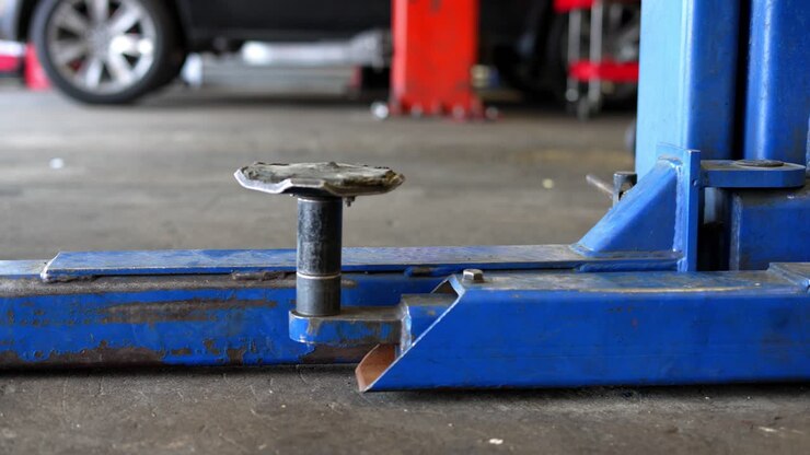 Slow panning right to left of distressed blue industrial automotive car truck lift jack in mechanics garage shop