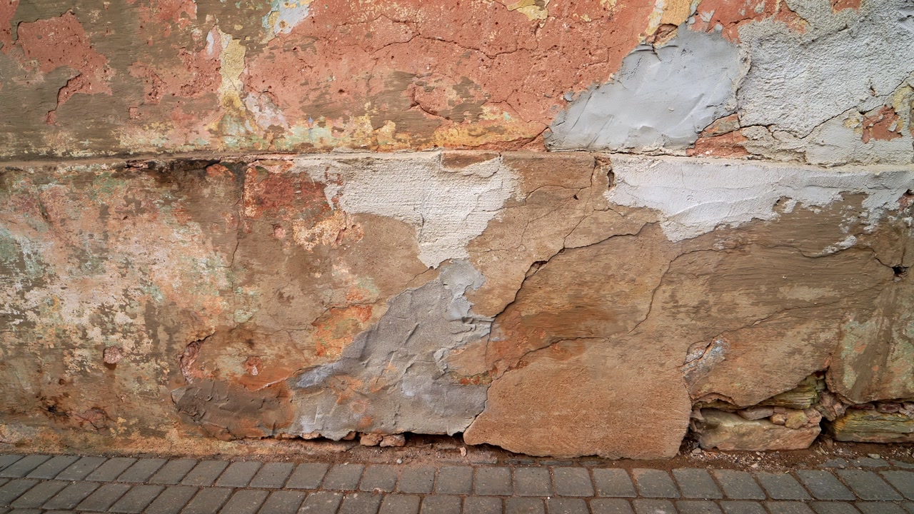 Close-up of a weathered exterior wall with peeling plaster, patch repairs, and flaking paint—grungy urban texture background with copy space.
