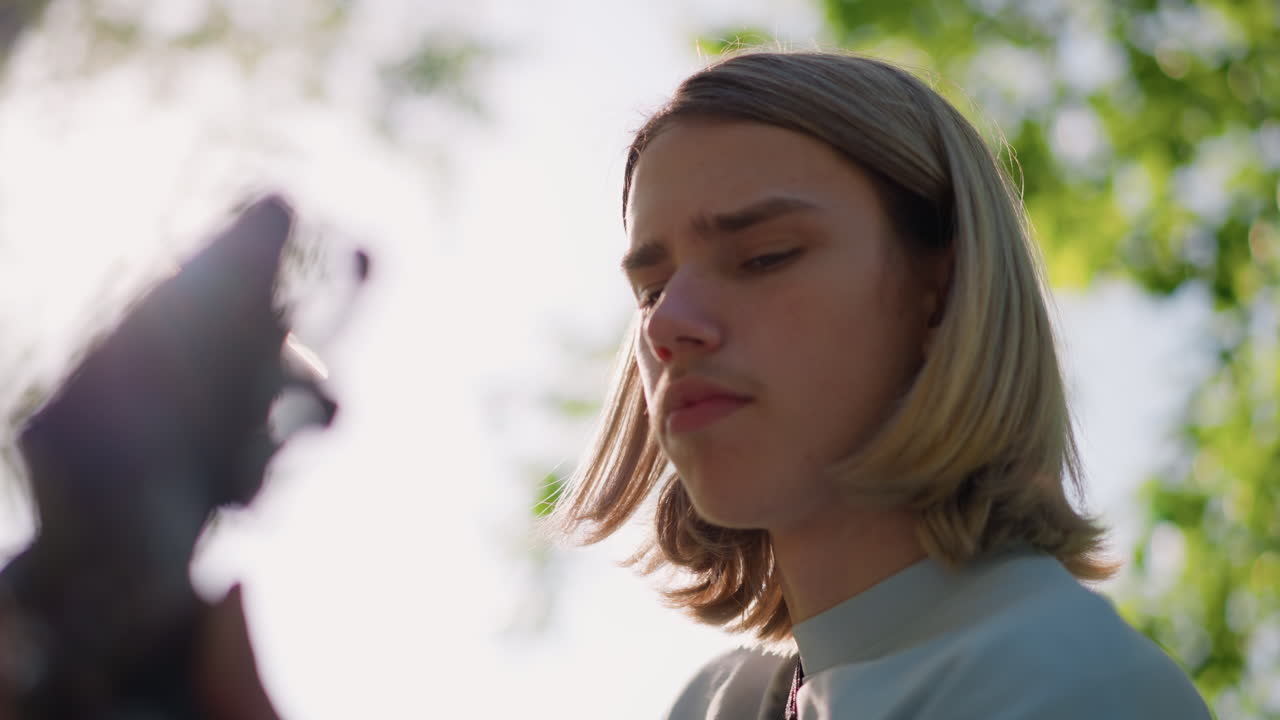 sunlit outdoor closeup of white guitarist student practicing acoustic guitar under leafy trees, thoughtful expression, soft backlight, natural bokeh, summer mood, candid portrait showcasing