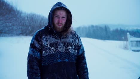 un hombre con una sudadera con capucha está de pie bajo la nieve que cae - toma estática