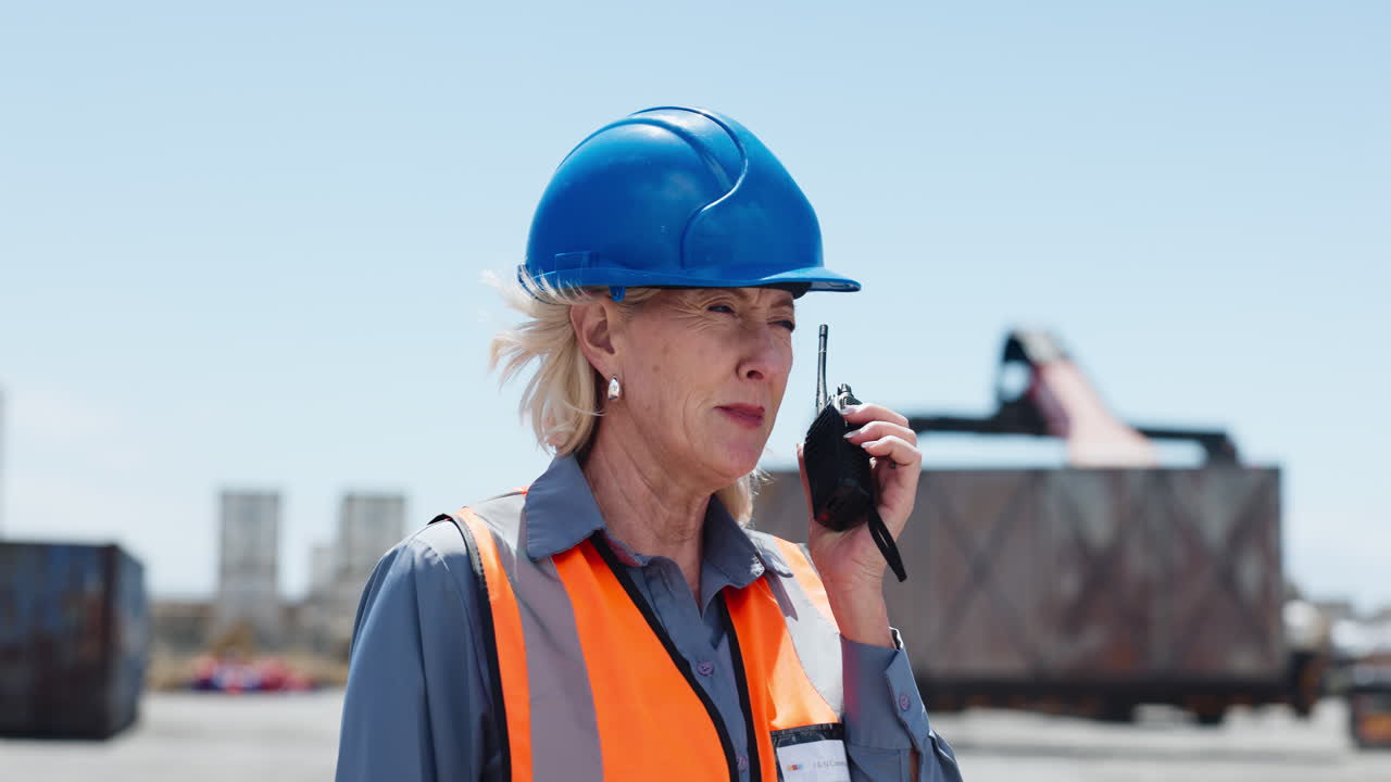 Donna matura con cappello e giubbotto di sicurezza che parla con un walkie-talkie