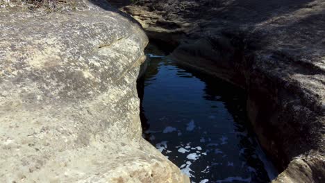 Following-water-flowing-downstream-as-it-follows-a-riverbed-over-stone-eroded-away-to-form-pools-along-the-stream