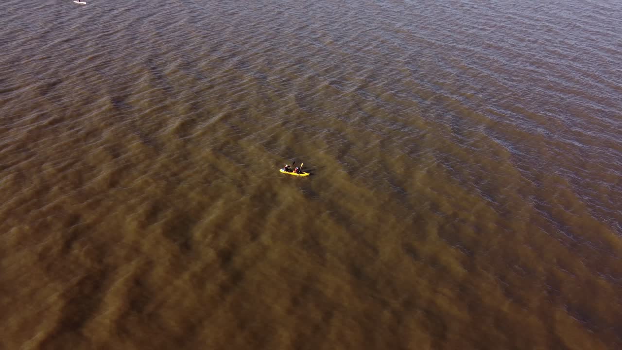 toma de órbita aérea de dos remeros remando en kayak en el río de la plata sucio cerca de buenos aires al atardecer