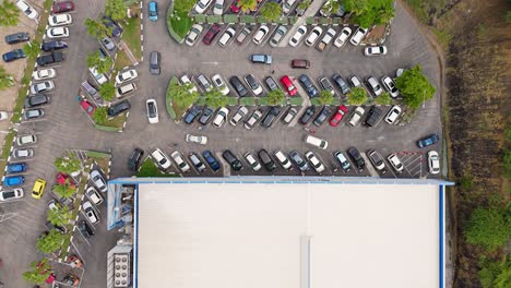 aerial top down static view of cars circling in parking lot of supermarket store