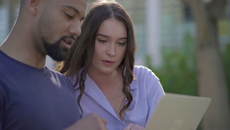 Young-man-and-pretty-woman-in-park-looking-at-laptop,-discussing