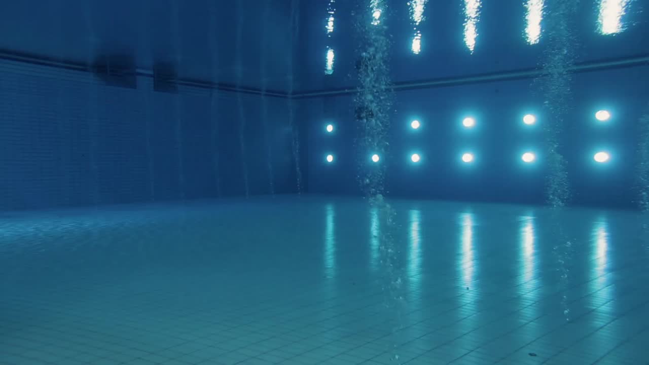 Underwater wide shot of a brightly lit Olympic diving pool, capturing, lights reflections and bubbles