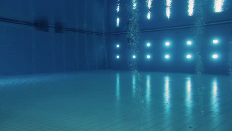 underwater wide shot of a brightly lit olympic diving pool, capturing, lights reflections and bubbles