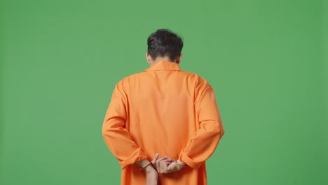 녹색 스크린 배경에 서 있는 동안 수갑을 벗으려고 노력하는 아시아 남성 죄수의 뒷면