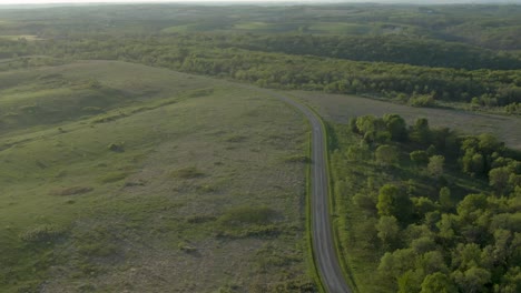 Toma-Aérea-De-Una-Carretera-Rural-Entre-Verdes-Prados-Y-Un-Espeso-Bosque-En-Las-Montañas-De-Wisconsin,-Ee.uu.