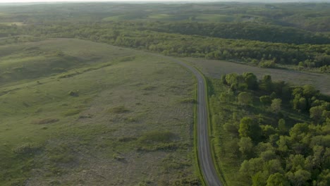 aerial shot of a country road between green meadows and a thick forest in the mountains of wisconsin, usa