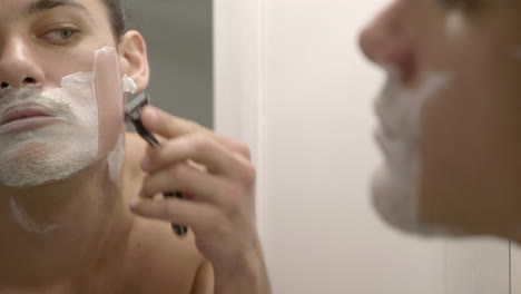 a man shaving his beard using a razor and some shaving cream - close up