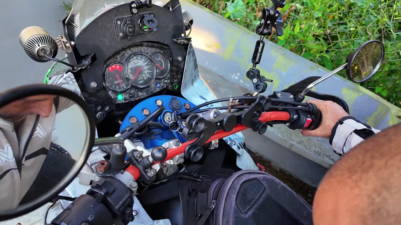 Plano detalhado em primeira pessoa de piloto acionando o interruptor de ignição e segurando o guidão de uma motocicleta de aventura, preparando-se para uma jornada pelas estradas da montanha