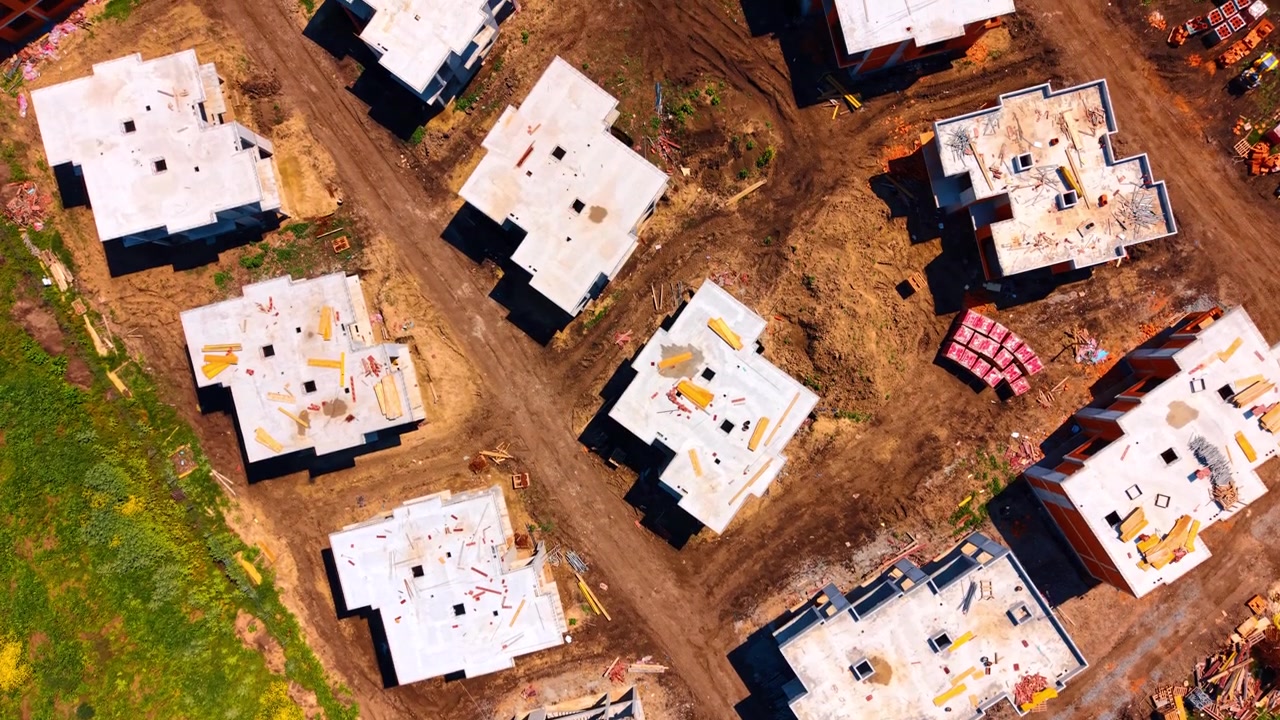 Top down aerial view of cottage construction site and materials. Straight down drone shot of concrete house structures under construction with bricks.