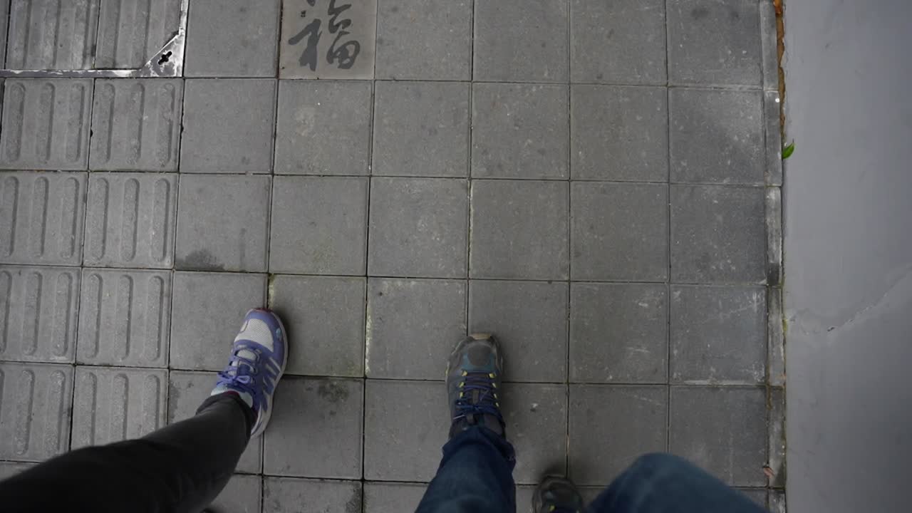 Top down close view of two pairs of feet walking over kanji lettered tiles on a street of Shanghai, China