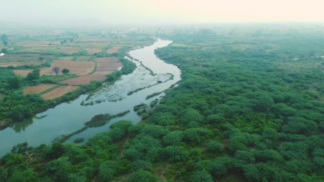 aerial drone shot of a flowing river through farmlands in gwalior , india