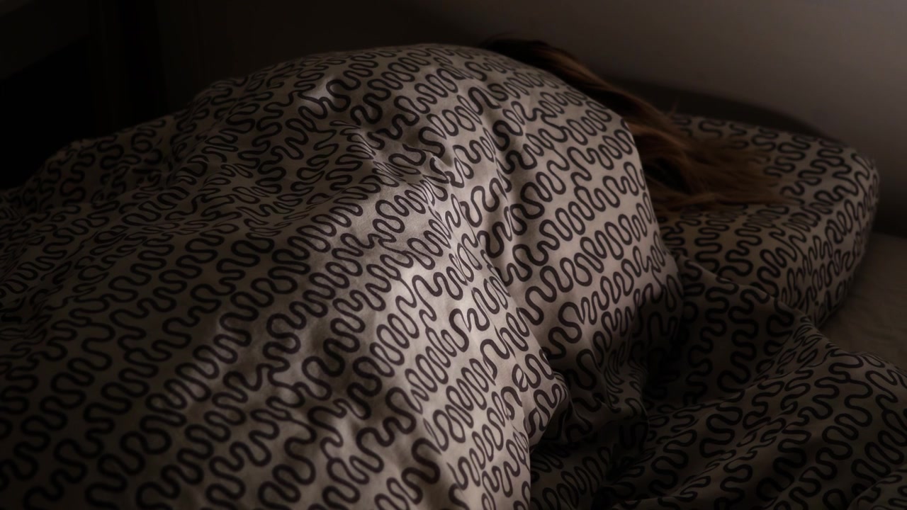 Persona che dorme sotto una coperta a fantasia in una camera da letto poco illuminata