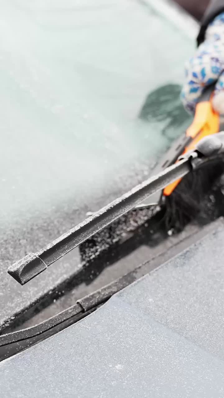 Frosne vinduesviskere og isglatte ruder, hvor en hånd med handske fjerner frost med en sneskraber, der viser vinterbilvedligeholdelse og forberedelse af udsyn. Vertikal nærbillede b-roll
