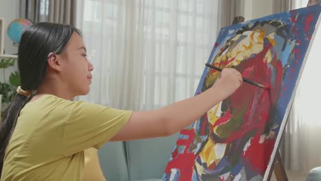 medium shot side view of an asian artist girl holding paintbrush mixed colour and painting a girl's ear on the canvas