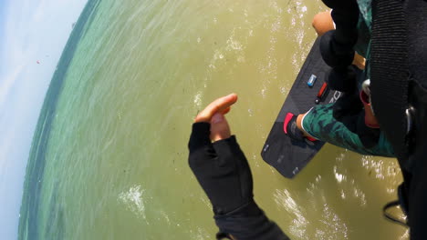 Kitesurfer-running-and-jumping-into-blue-ocean-water-with-red-board,-POV-vertical