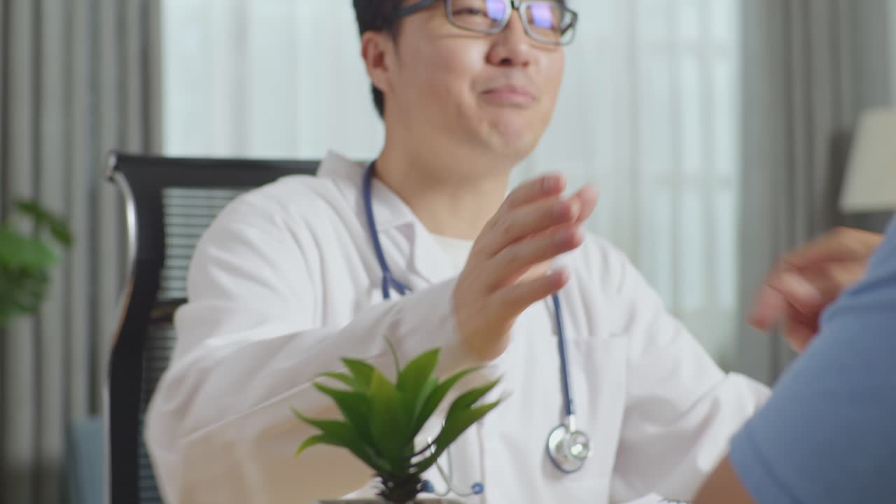아시아 남성 의사가 클리닉에서 한 남성 환자와 악수를 하고 대화하는 장면