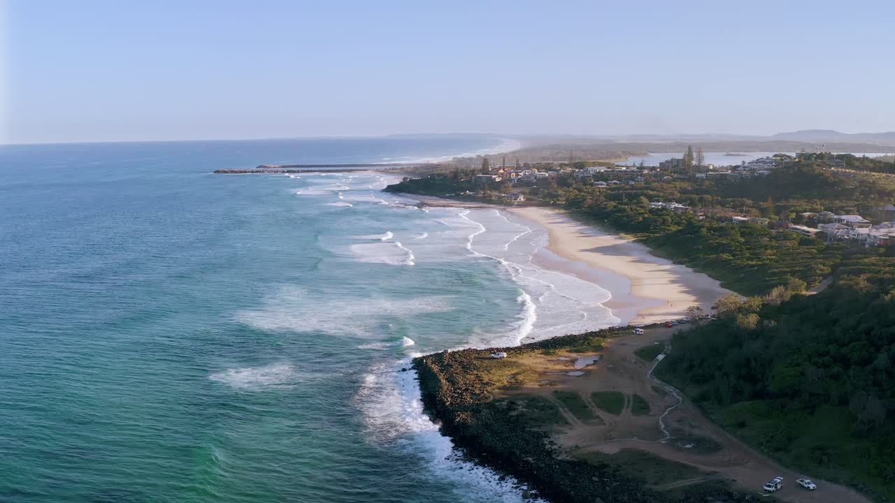 Aerial view of waves crashing onto the sandy coastline of Ham Tien Beach, Mui Ne, Vietnam. Lush green hills and a peaceful environment provide a tranquil backdrop to the stunning beach scene
