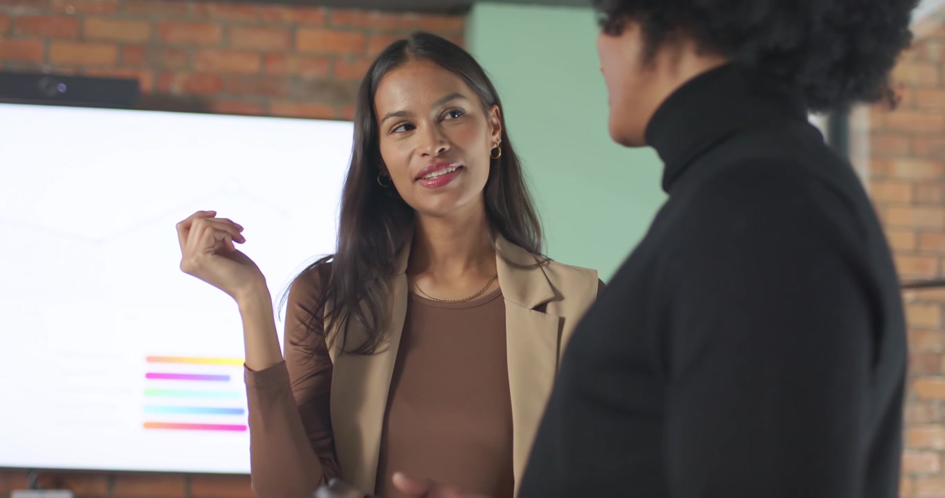 Colegas afro-americanos, mulher revisando gráfico de barras no escritório enquanto homem fala segurando o telefone.