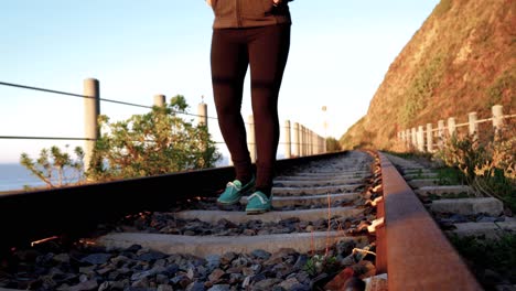 Lonely-woman-walking-on-old-train-tracks-next-to-the-ocean-in-Wilderness,-South-Africa