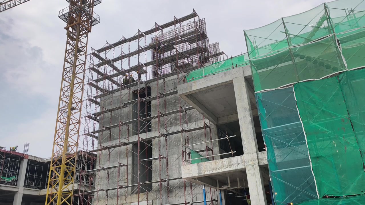 Konstruksi gedung bertingkat tinggi sedang berlangsung. Tindakan keselamatan ketat sangat ditegakkan di lokasi. Material berat tertata rapi untuk alur kerja yang efisien