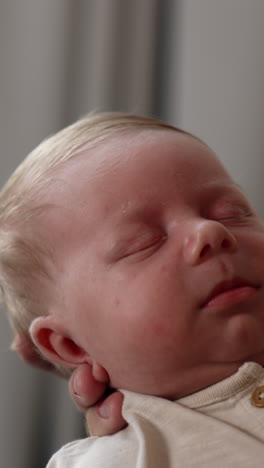 caucasian newborn looking unhappy. baby boy sleeping in parent's hands. close up. vertical video