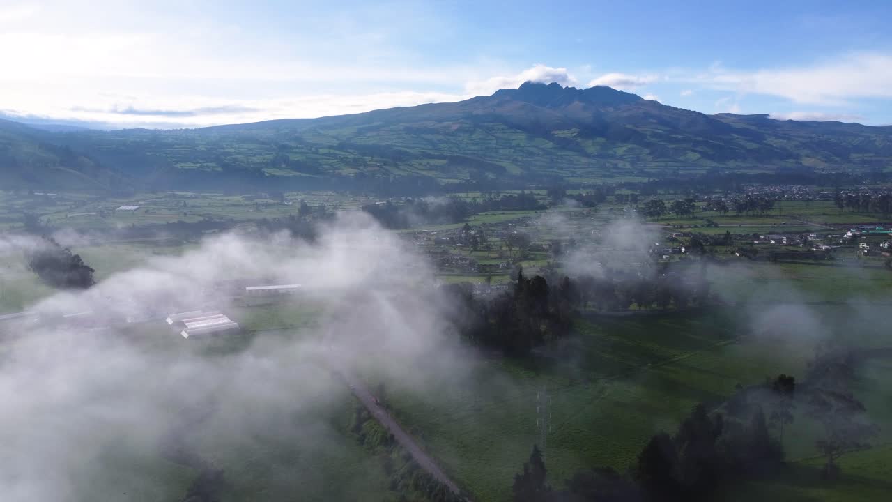 clip de drone en movimiento lento sobre un campo verde y un pueblo con el volcán volcán rumiñahui en el fondo en neblina, machachi en ecuador