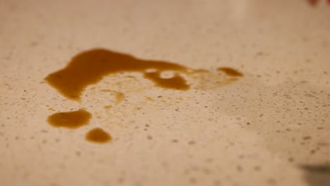 a person cleans a coffee spill on a speckled countertop using a yellow cloth under warm lighting