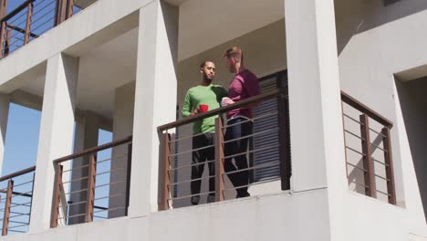 multi ethnic gsy male couple drinking coffee on balcony in sun