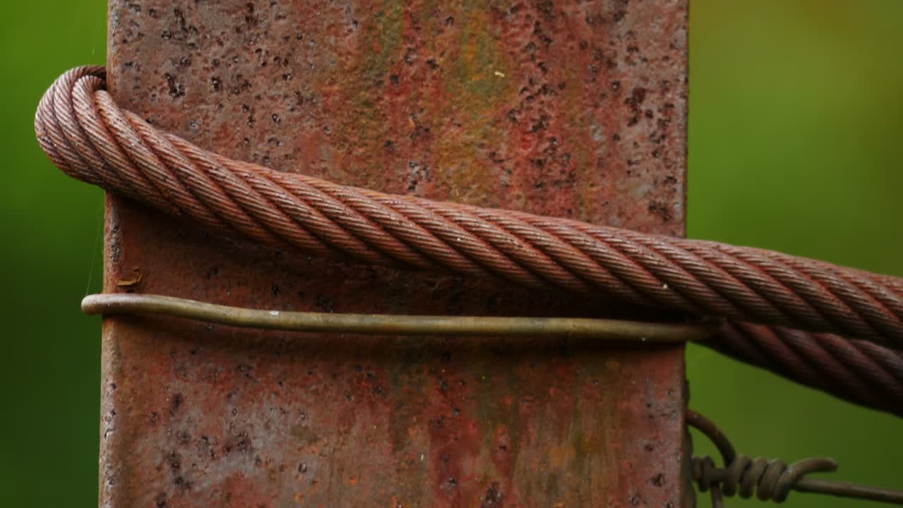 textura macro oxidada, pilar de hierro con alambre, cable de acero y barras metálicas, enfoque superficial contra fondo verde